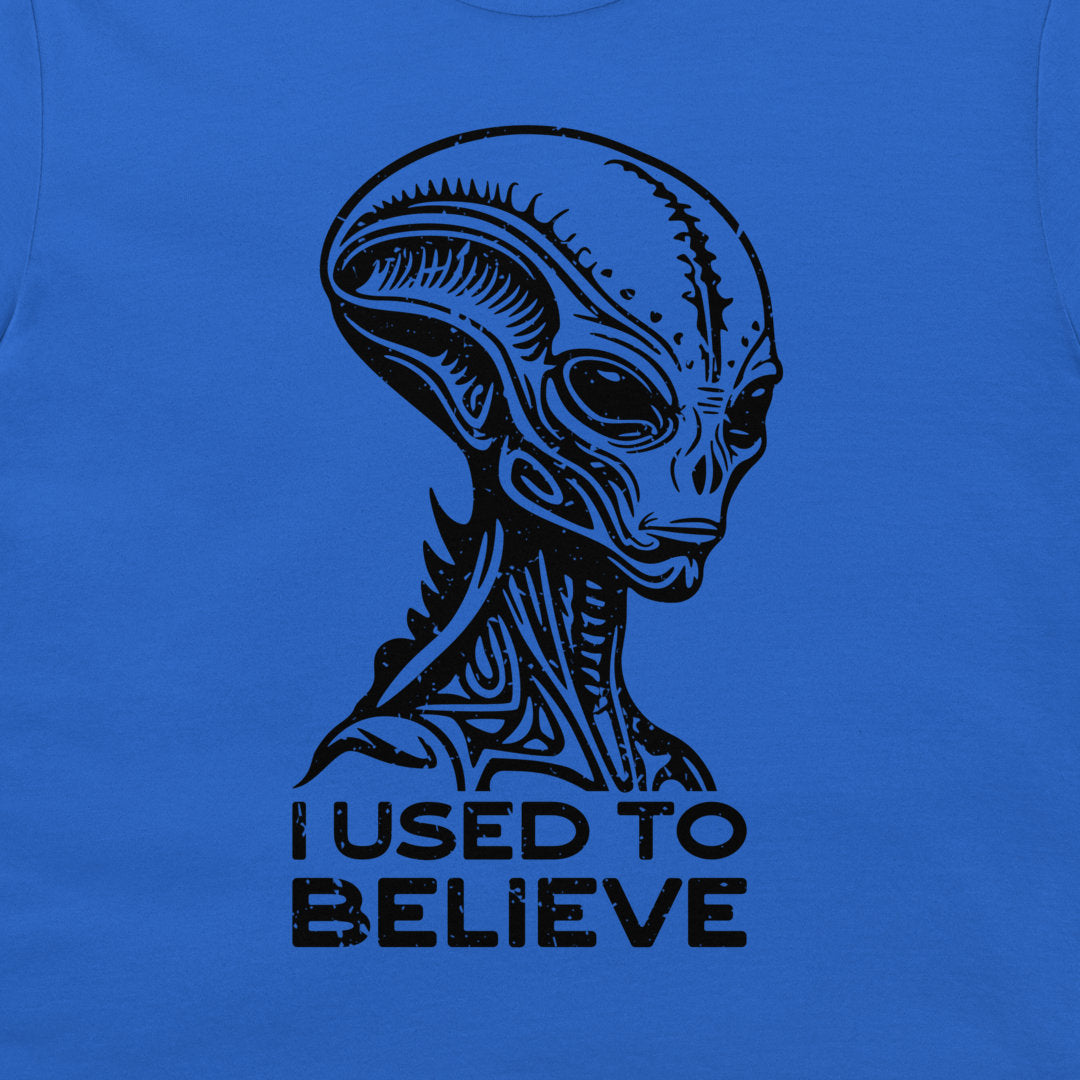 A close-up of a blue t-shirt featuring a black graphic of a classic sci-fi alien head with the text 'I USED TO BELIEVE' printed below it.