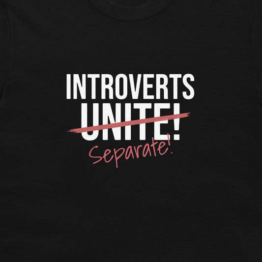A close-up of a black t-shirt featuring a graphic print that reads 'INTROVERTS UNITE!' in white block letters, crossed out with a red scribble, with 'Separate!' written below in red script.