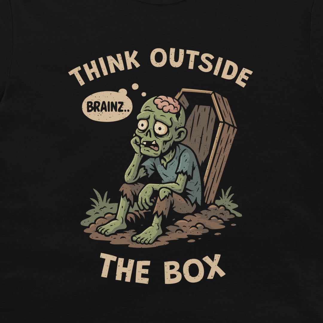 A black graphic t-shirt featuring a cartoon zombie sitting next to a coffin with the text 'THINK OUTSIDE THE BOX' and a thinking bubble that says 'BRAINZ.