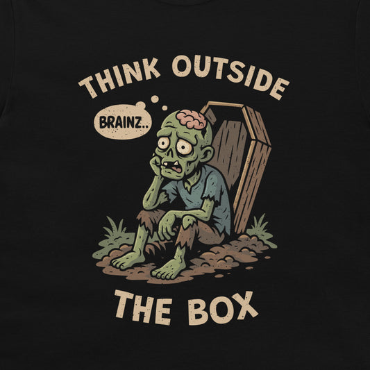 A black graphic t-shirt featuring a cartoon zombie sitting next to a coffin with the text 'THINK OUTSIDE THE BOX' and a thinking bubble that says 'BRAINZ.