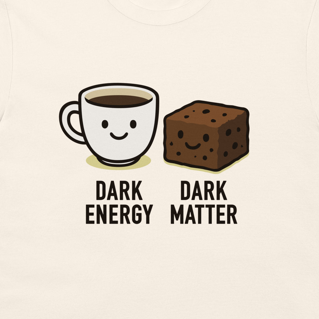 A close-up of a light cream-colored garment, likely a t-shirt, featuring a cartoon graphic of a smiling coffee cup labeled 'DARK ENERGY' next to a smiling brownie labeled 'DARK MATTER'.