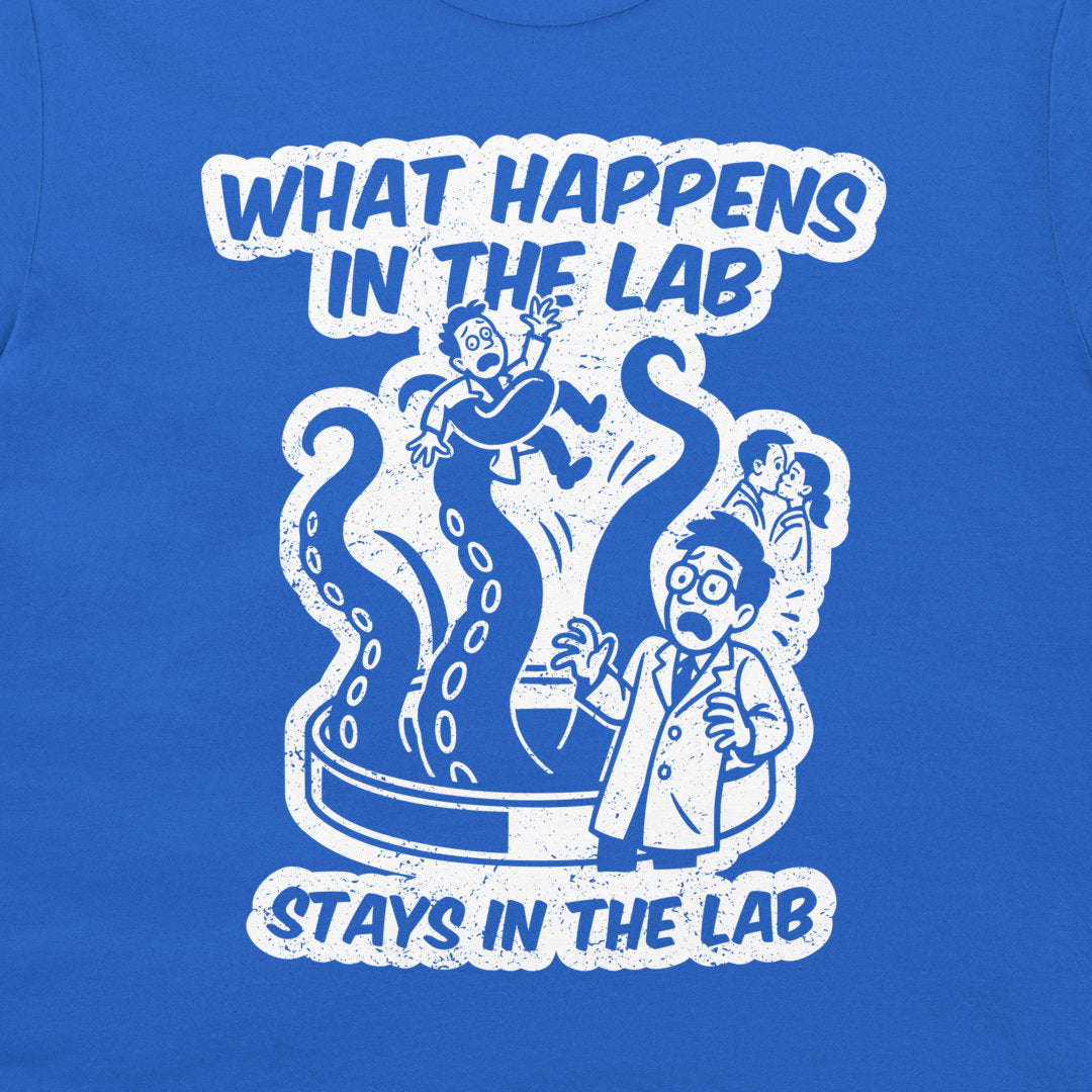 A close-up of a royal blue t-shirt featuring a white distressed graphic print with the text 'WHAT HAPPENS IN THE LAB STAYS IN THE LAB' and a cartoon illustration of lab accidents.