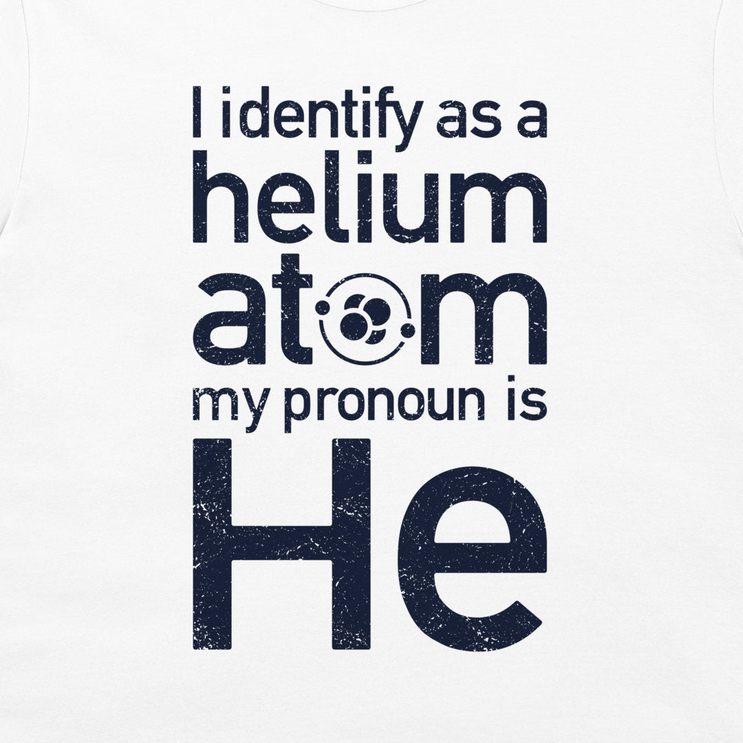 White t-shirt featuring a dark navy blue distressed graphic print that reads 'I identify as a helium atom my pronoun is He' with an atom symbol inside the letter 'o' in 'atom'.