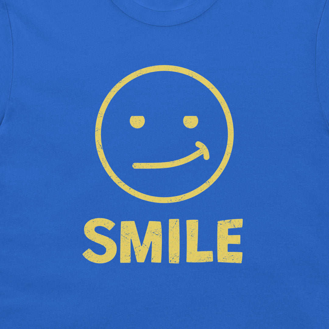 A close-up of a royal blue t-shirt, featuring a distressed yellow graphic of a smiling face and the word 'SMILE' printed below it.