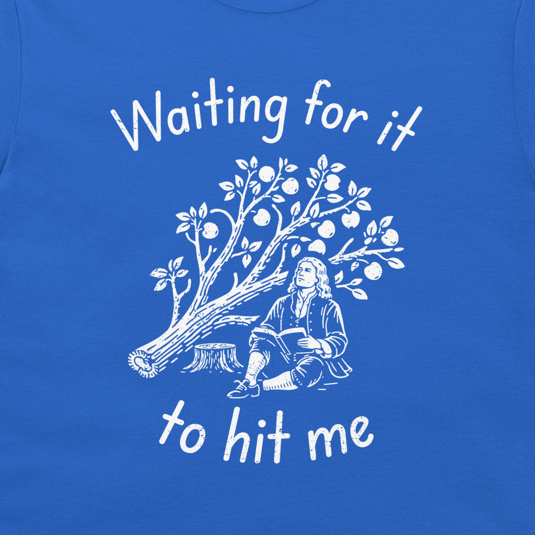 A close-up of a royal blue t-shirt featuring a white graphic print of a tree with fruit and a historical figure sitting beneath it, with the text 'Waiting for it to hit me' written in white script.