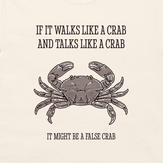A close-up of a cream-colored garment, likely a t-shirt, featuring a black graphic print of a crab and the humorous text 'IF IT WALKS LIKE A CRAB AND TALKS LIKE A CRAB IT MIGHT BE A FALSE CRAB'.