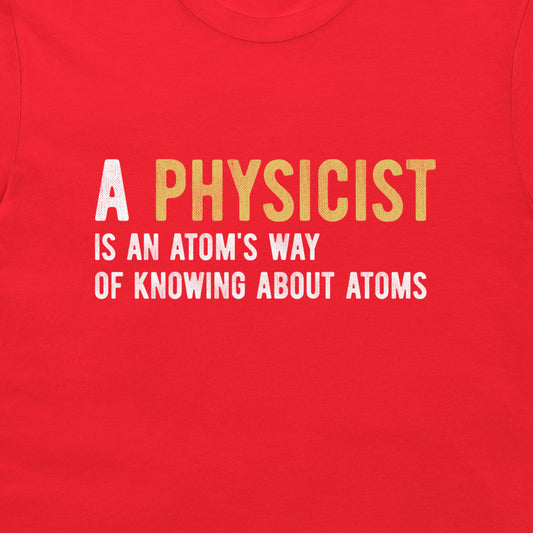 A close-up of a bright red t-shirt featuring a printed graphic with the text 'A PHYSICIST IS AN ATOM'S WAY OF KNOWING ABOUT ATOMS' in white and yellow lettering.