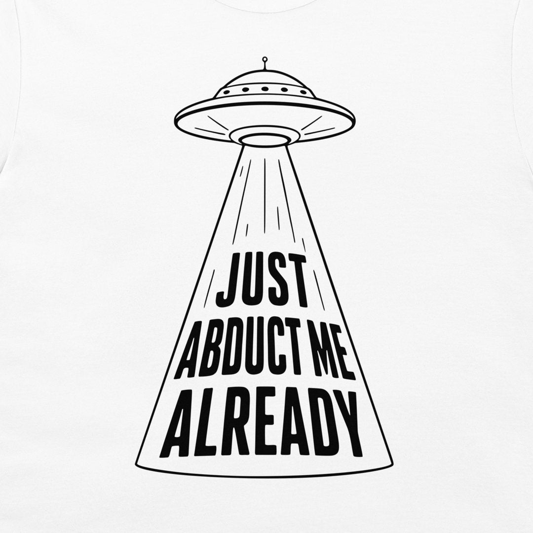 A white t-shirt featuring a black graphic of a classic flying saucer UFO casting a beam of light with the bold text 'JUST ABDUCT ME ALREADY'.