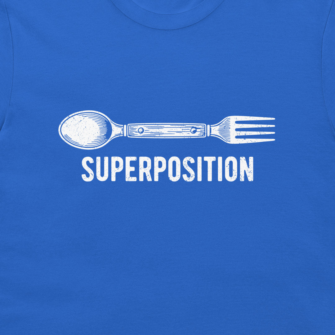 A close-up of a royal blue t-shirt featuring a white graphic of a spoon fused with a fork, with the word 'SUPERPOSITION' printed below in a distressed white font.
