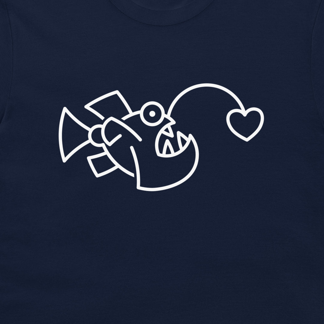 A close-up of a black t-shirt, featuring a white line art graphic of an angler fish with a heart-shaped lure.