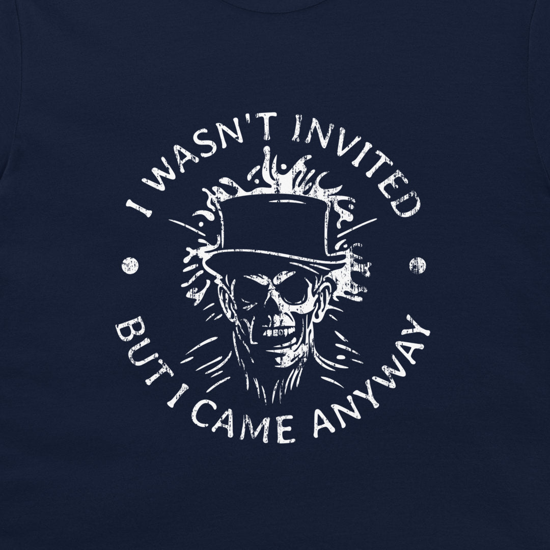 A close-up of a navy blue t-shirt, featuring a distressed white graphic print of a skull in a top hat with flames, surrounded by the text 'I WASN'T INVITED BUT I CAME ANYWAY'.