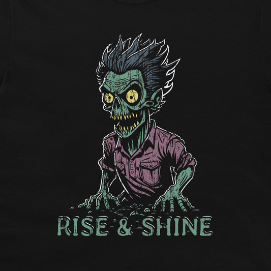 A black t-shirt featuring a graphic of a green zombie with yellow eyes, wild hair, and a purple shirt, with the text 'RISE & SHINE' written below in a distressed teal font.