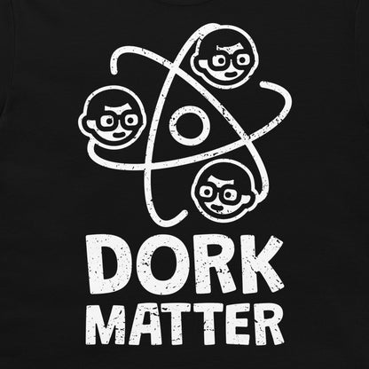A close-up of a black t-shirt, featuring a white distressed graphic of three cartoon dork faces orbiting an atom symbol above the text 'DORK MATTER'.