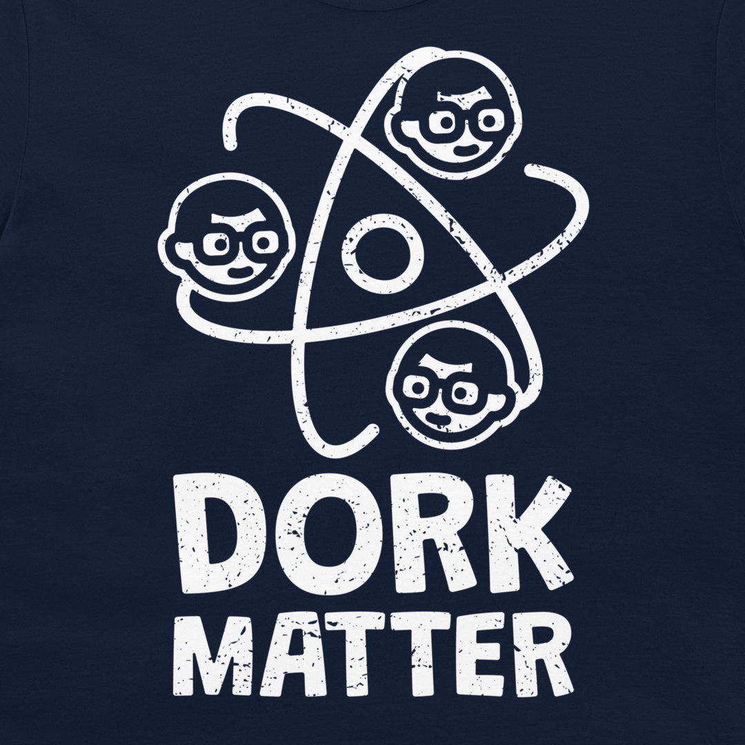 A close-up of a navy blue t-shirt featuring a white distressed graphic of three cartoon faces orbiting an atom symbol above the text 'DORK MATTER'.