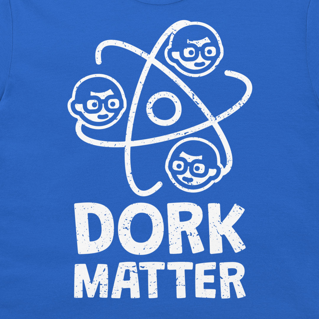 A close-up of a blue T-shirt featuring a white distressed graphic of three cartoon faces orbiting a circle, with the text 'DORK MATTER' printed below.