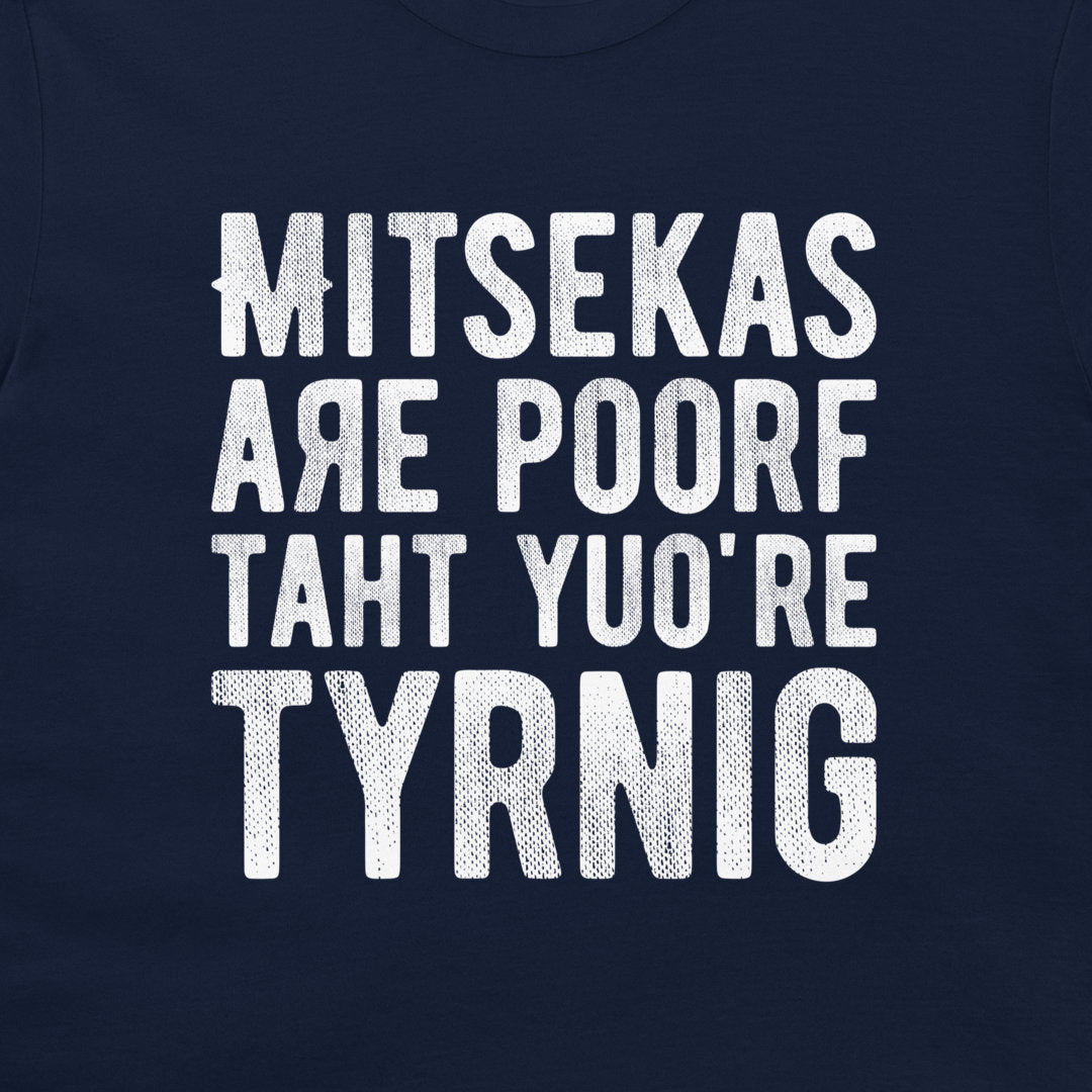 A close-up of a navy blue t-shirt featuring a distressed white typographic print that reads 'MITSEKAS ARE POORF TAHT YU'O RE TYRNIG'.