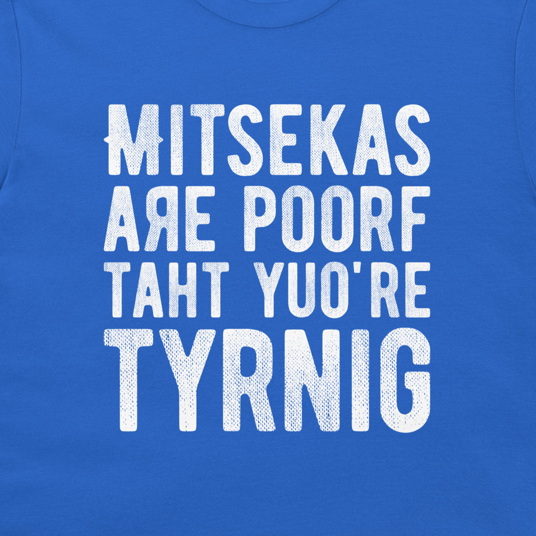 A close-up of a royal blue t-shirt featuring a distressed white text graphic that reads 'MITSEKAS ARE POORF TAHT YU'O RE TYRNIG' in a stylized, blocky font.
