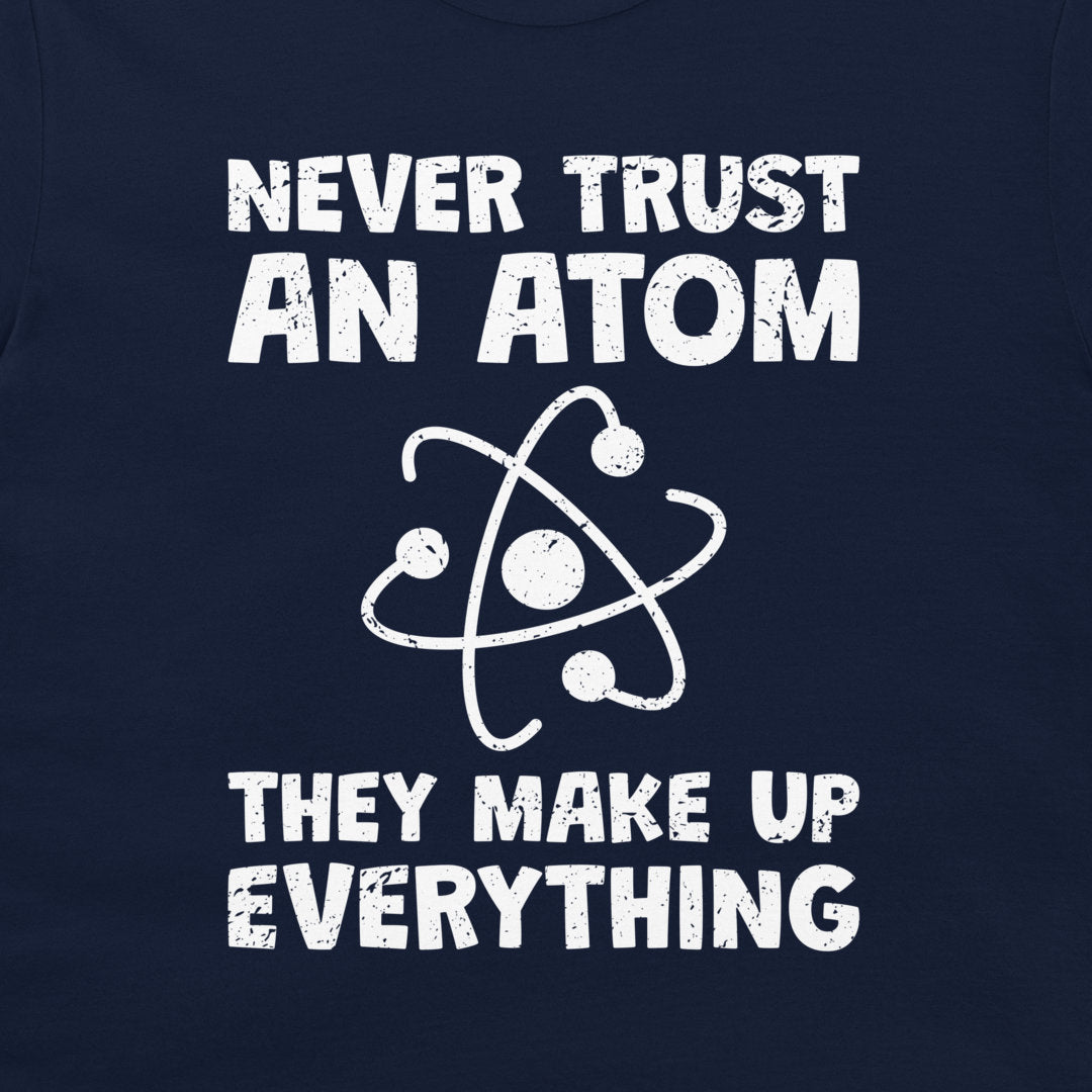A close-up of a navy blue garment, likely a t-shirt, featuring a white distressed graphic print that reads 'NEVER TRUST AN ATOM THEY MAKE UP EVERYTHING' with an atom symbol in the center.