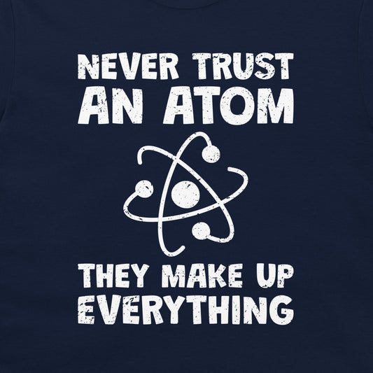 A close-up of a navy blue garment, likely a t-shirt, featuring a white distressed graphic print that reads 'NEVER TRUST AN ATOM THEY MAKE UP EVERYTHING' with an atom symbol in the center.