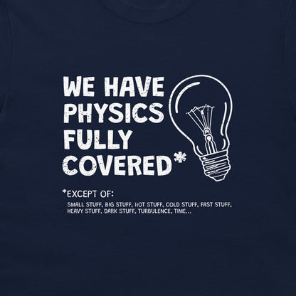 A close-up of a navy blue t-shirt featuring a white graphic print that reads 'WE HAVE PHYSICS FULLY COVERED' next to a lightbulb outline, with a humorous exception list below.