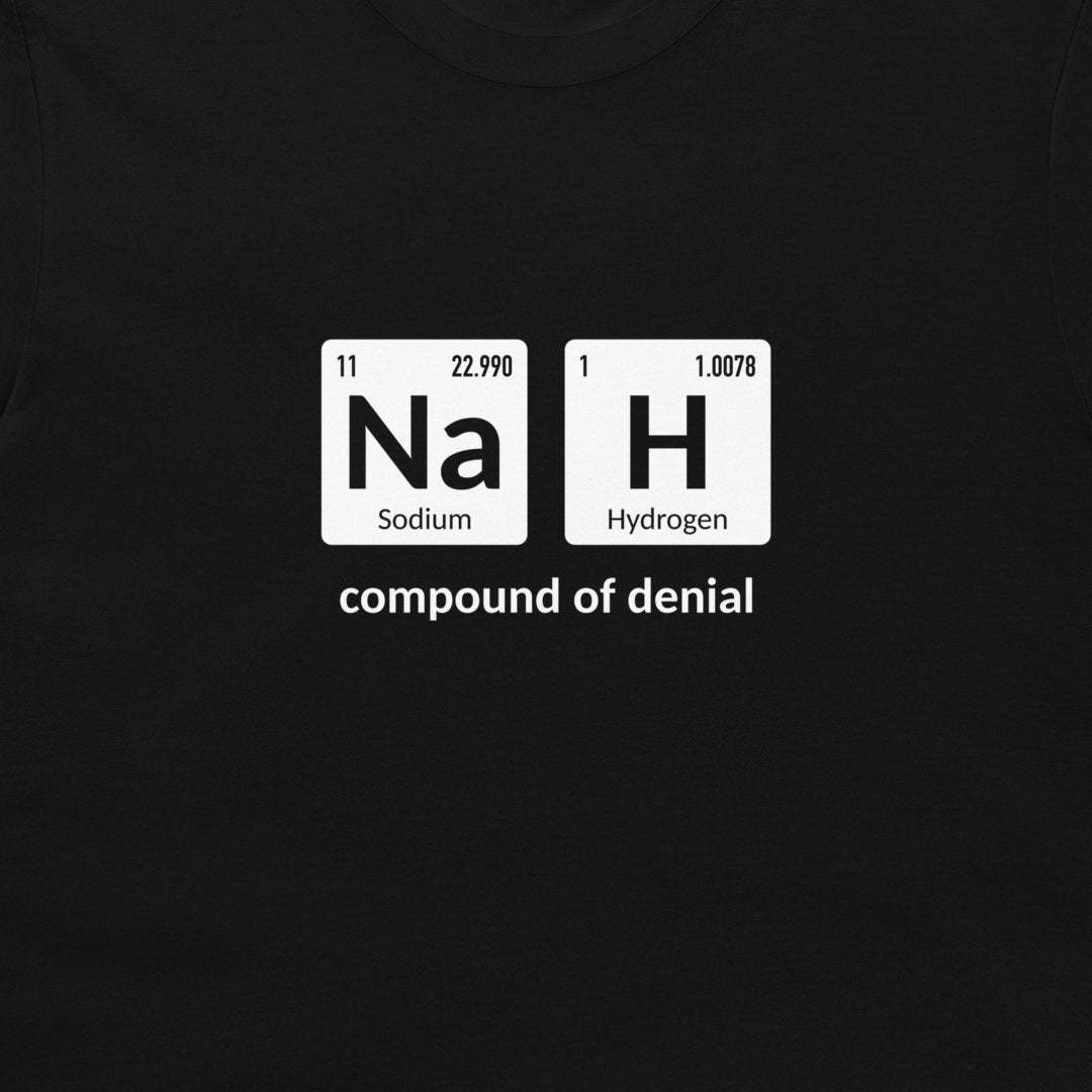 A close-up of a black garment, likely a t-shirt, featuring a white graphic print of periodic table elements 'Na' and 'H' with the text 'compound of denial' underneath.