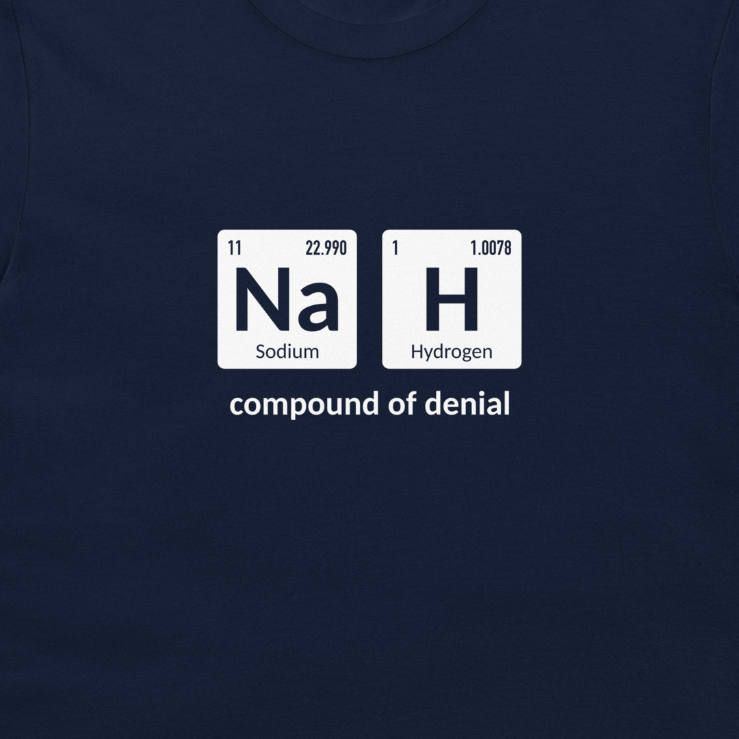 A close-up of a navy blue t-shirt featuring a white graphic print that reinterprets the periodic table elements 'Na' (Sodium) and 'H' (Hydrogen) as the 'compound of denial'.