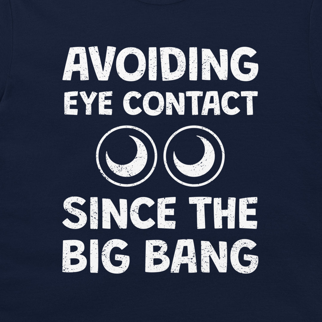 A close-up of a navy blue t-shirt featuring a white distressed graphic that reads 'AVOIDING EYE CONTACT SINCE THE BIG BANG' with two crescent moon and circle eye designs.