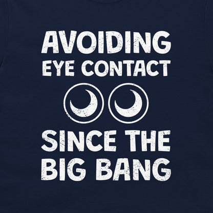 A close-up of a navy blue t-shirt featuring a white distressed graphic that reads 'AVOIDING EYE CONTACT SINCE THE BIG BANG' with two crescent moon and circle eye designs.