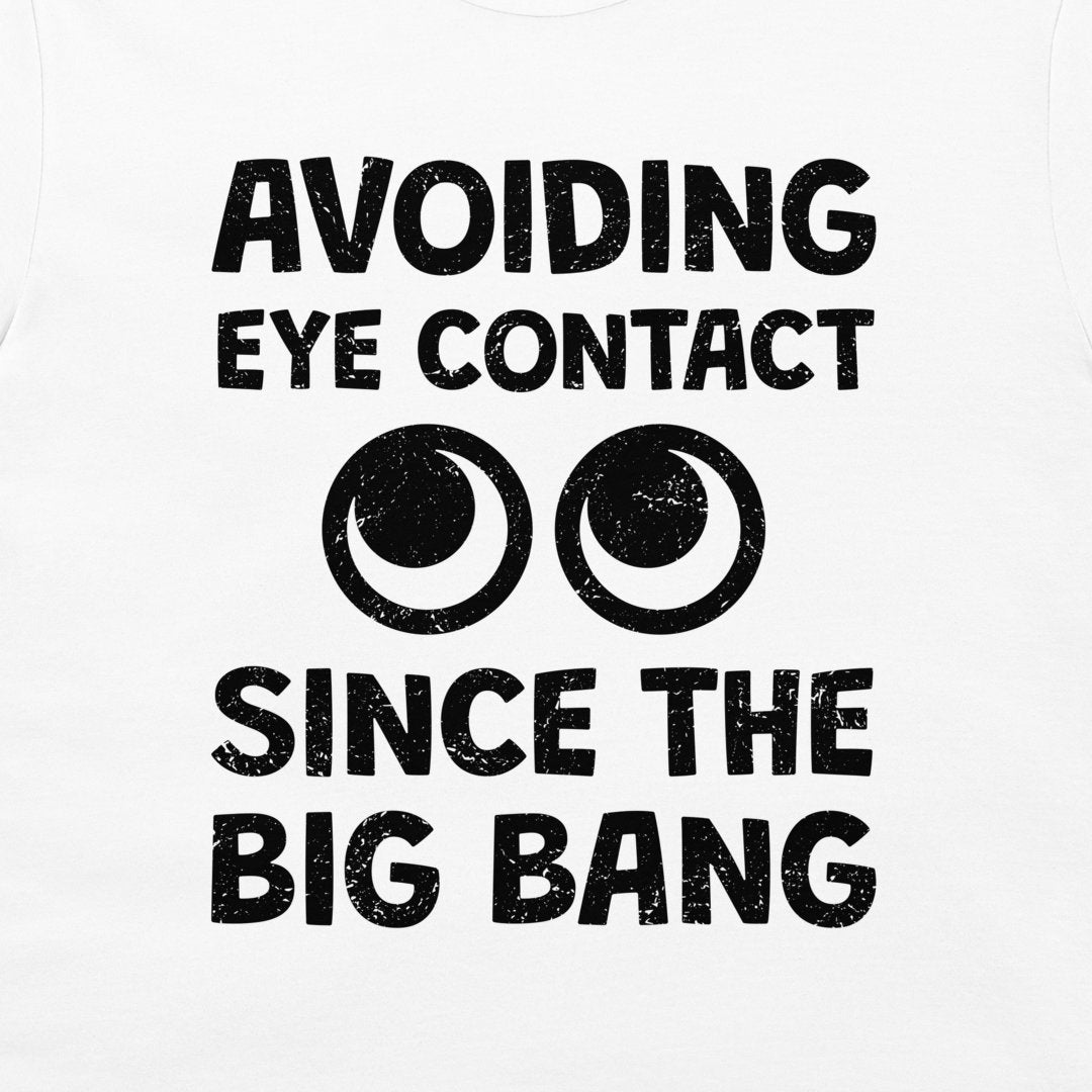White t-shirt with a black distressed graphic print that reads 'AVOIDING EYE CONTACT SINCE THE BIG BANG' with two cartoon eyes in the center.