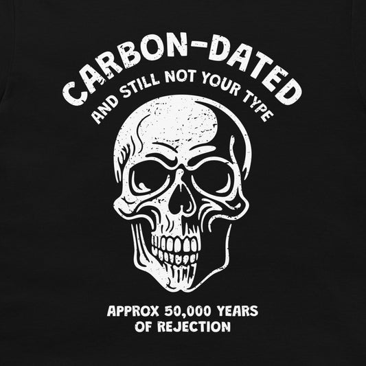 A navy blue graphic print featuring a white distressed skull and the text 'CARBON-DATED AND STILL NOT YOUR TYPE' and 'APPROX 50,000 YEARS OF REJECTION'.