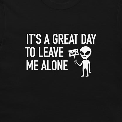 A close-up of a black t-shirt featuring a white graphic print that reads 'IT'S A GREAT DAY TO LEAVE ME ALONE' next to a cartoon alien holding a 'NOPE' sign.