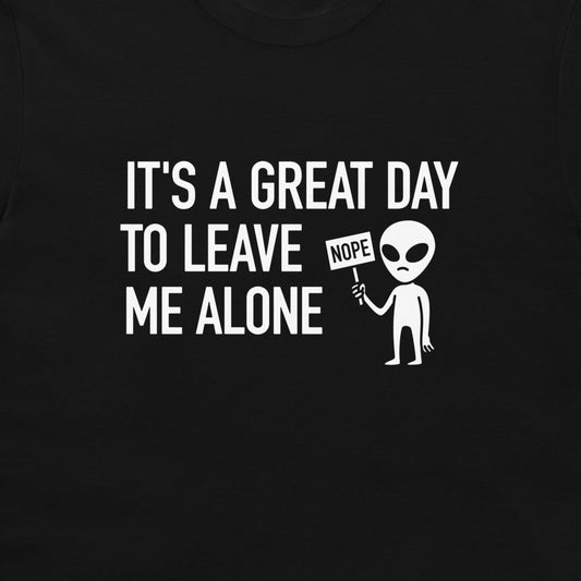 A close-up of a black t-shirt featuring a white graphic print that reads 'IT'S A GREAT DAY TO LEAVE ME ALONE' next to a cartoon alien holding a 'NOPE' sign.