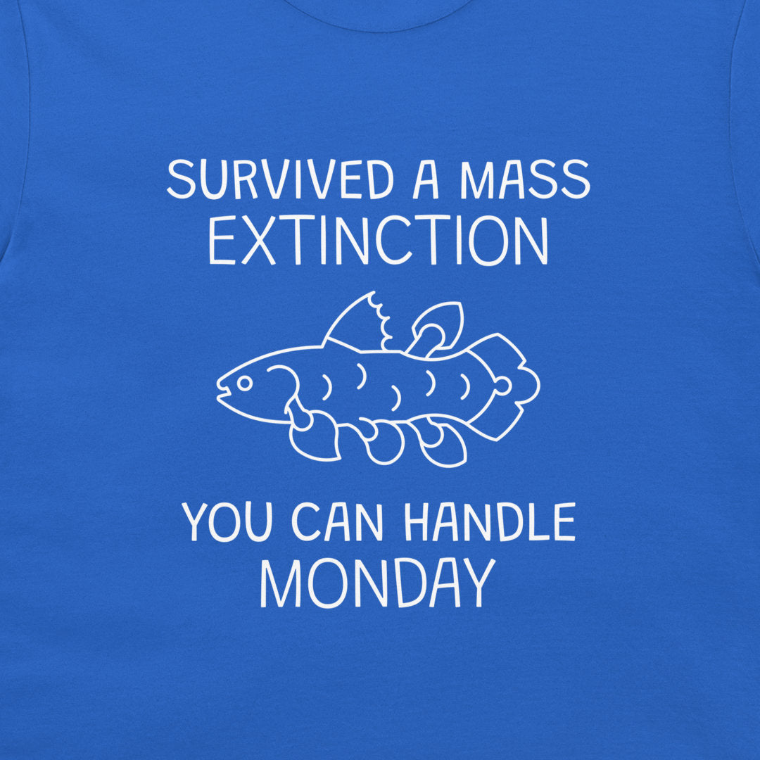 A close-up of a blue T-shirt with a white graphic print that reads 'SURVIVED A MASS EXTINCTION YOU CAN HANDLE MONDAY' with a simple fish illustration in the center.