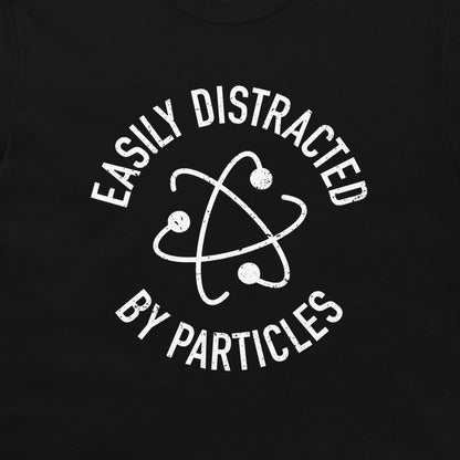 A close-up of a t-shirt, featuring a distressed white graphic print of an atom symbol with the text 'EASILY DISTRACTED BY PARTICLES'.