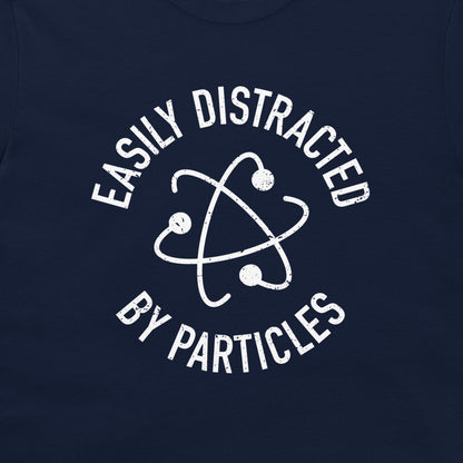 A close-up of a navy blue t-shirt, featuring a distressed white graphic of an atom symbol with the text 'EASILY DISTRACTED BY PARTICLES'.