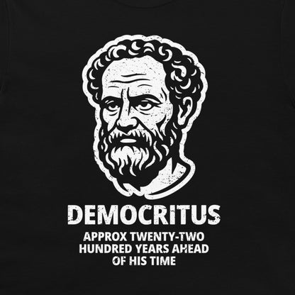 A black t-shirt featuring a white distressed graphic of a bearded man's portrait labeled 'DEMOCRITUS' with the text 'APPROX TWENTY-TWO HUNDRED YEARS AHEAD OF HIS TIME' below.