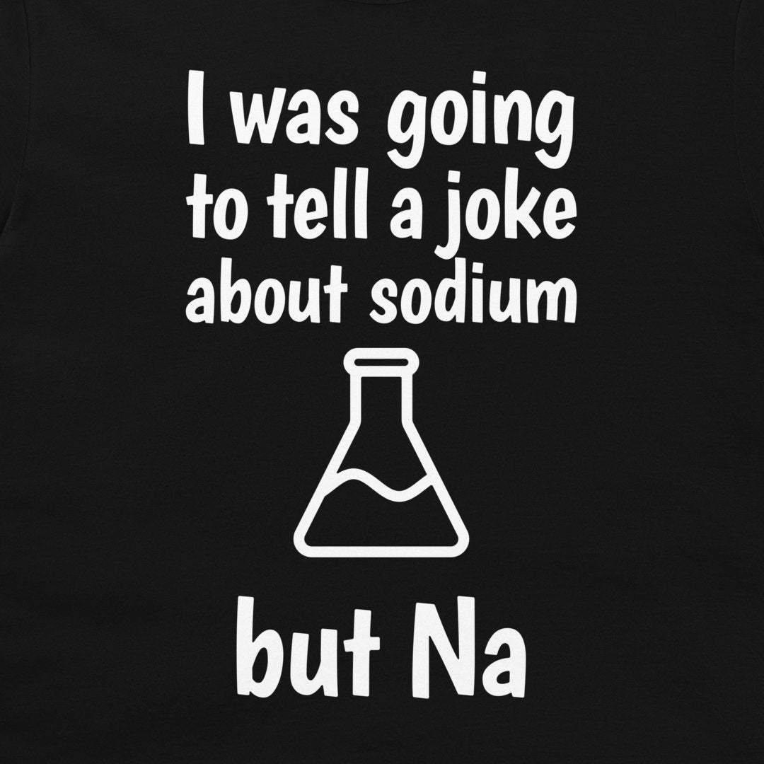 A close-up of a black t-shirt, featuring a white printed graphic with the text 'I was going to tell a joke about sodium but Na' and a simple beaker outline.