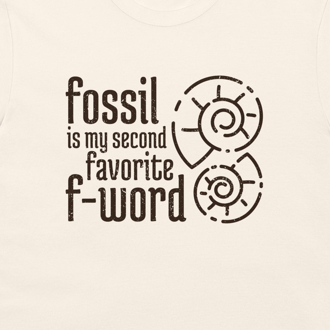 A close-up of a light cream-colored t-shirt featuring a dark brown graphic print that reads 'fossil is my second favorite f-word' alongside two spiral ammonite illustrations.