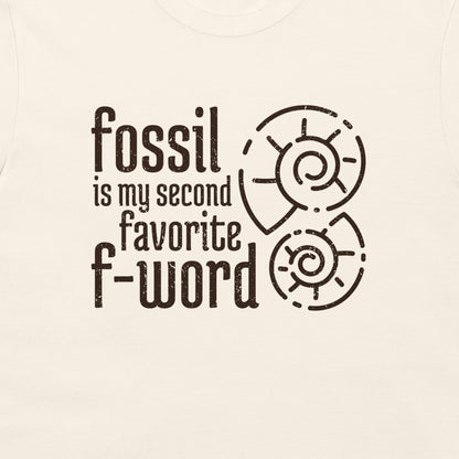 A close-up of a light cream-colored t-shirt featuring a dark brown graphic print that reads 'fossil is my second favorite f-word' alongside two spiral ammonite illustrations.