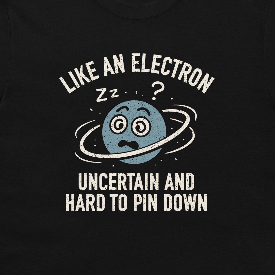 A close-up of a black t-shirt featuring a graphic print of a blue planet with a ring around it, looking confused, with the text 'LIKE AN ELECTRON' above and 'UNCERTAIN AND HARD TO PIN DOWN' below in distressed white lettering.