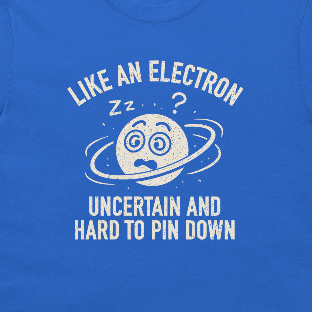 A close-up of a blue T-shirt featuring a white distressed graphic of a confused planet with a ring and the text 'LIKE AN ELECTRON UNCERTAIN AND HARD TO PIN DOWN' with 'zz' and a question mark.