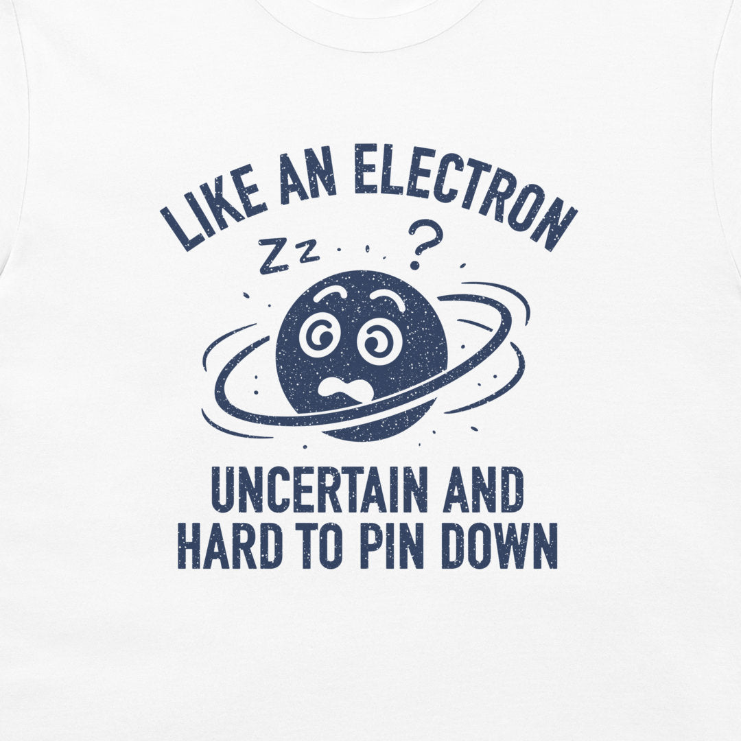 A close-up of a white garment, likely a t-shirt, featuring a dark navy blue graphic print. The design shows a cartoon planet with a worried face, a ring, 'zz' marks, and a question mark, surrounded by the text 'LIKE AN ELECTRON UNCERTAIN AND HARD TO PIN DOWN'.