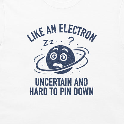 A close-up of a white garment, likely a t-shirt, featuring a dark navy blue graphic print. The design shows a cartoon planet with a worried face, a ring, 'zz' marks, and a question mark, surrounded by the text 'LIKE AN ELECTRON UNCERTAIN AND HARD TO PIN DOWN'.
