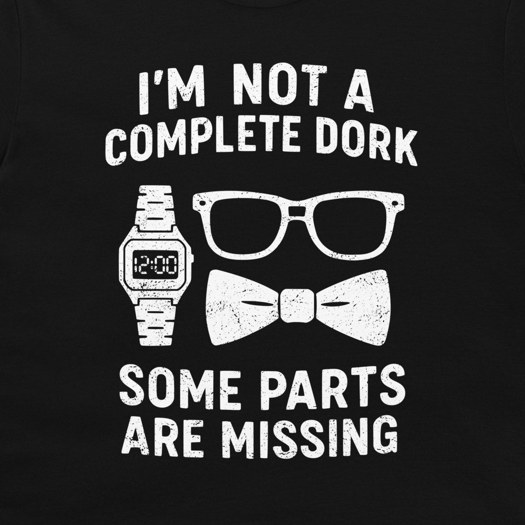 A close-up of a black  t-shirt, featuring a white distressed graphic print. The text reads 'I'M NOT A COMPLETE DORK' above an illustration of a digital watch, eyeglasses, and a bow tie, and 'SOME PARTS ARE MISSING' below.