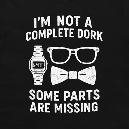 A close-up of a black  t-shirt, featuring a white distressed graphic print. The text reads 'I'M NOT A COMPLETE DORK' above an illustration of a digital watch, eyeglasses, and a bow tie, and 'SOME PARTS ARE MISSING' below.