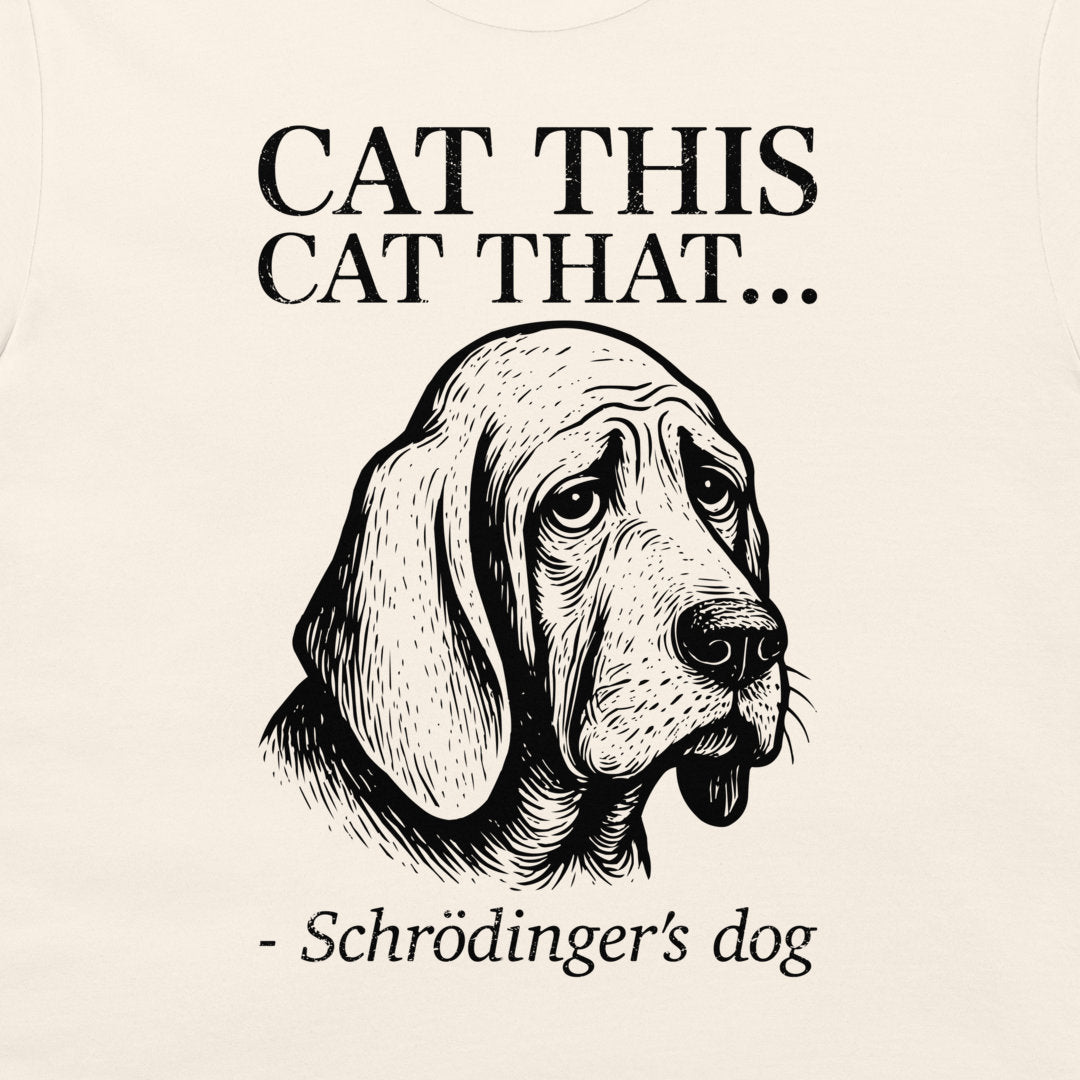 A close-up of a cream-colored t-shirt, featuring a black graphic print of a sad bloodhound Schrödinger's dog with the text 'CAT THIS CAT THAT.