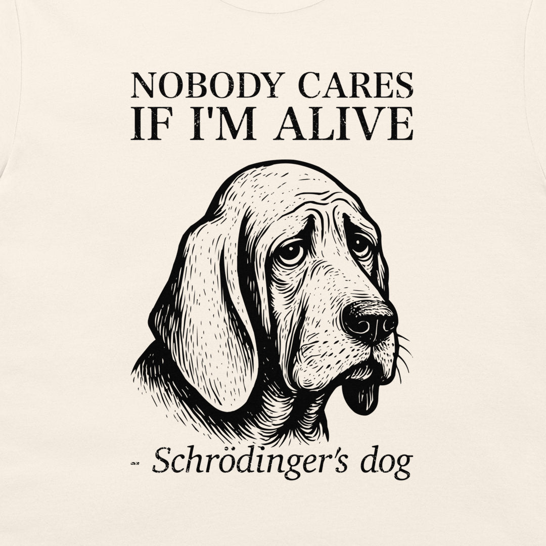 A close-up of a cream-colored t-shirt featuring a black graphic print of a sad-looking bloodhound dog with the text 'NOBODY CARES IF I'M ALIVE' and '- Schrödinger's dog'.
