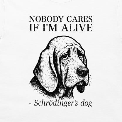 A close-up of a cream-colored t-shirt featuring a black graphic print of a sad-looking bloodhound dog with the text 'NOBODY CARES IF I'M ALIVE' and '- Schrödinger's dog'.