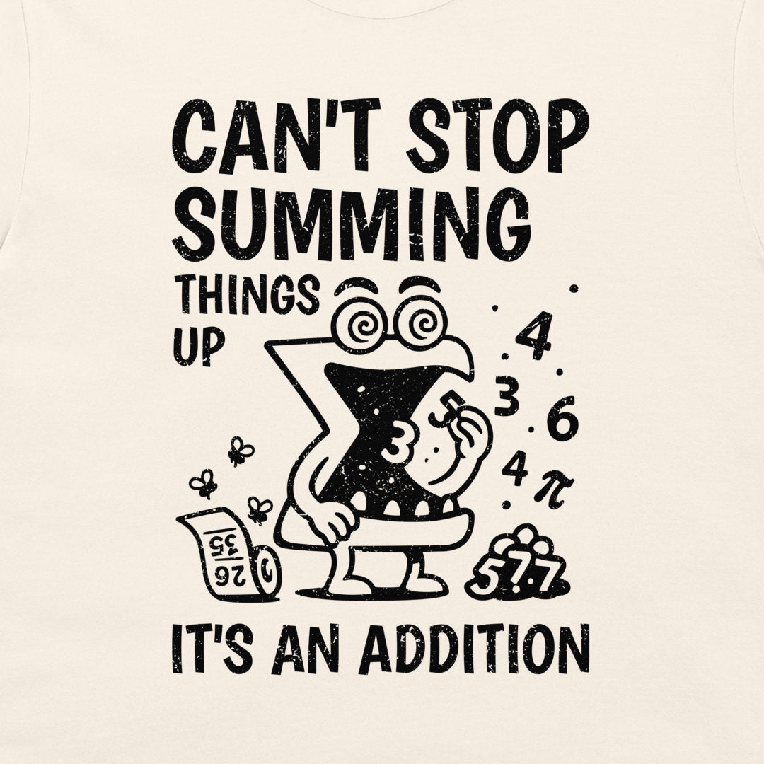 A close-up of a cream-colored t-shirt featuring a black graphic print. The design shows a cartoon letter 'X' character in a toilet bowl with the text 'CAN'T STOP SUMMING THINGS UP' above and 'IT'S AN ADDITION' below, surrounded by numbers and a calculator.