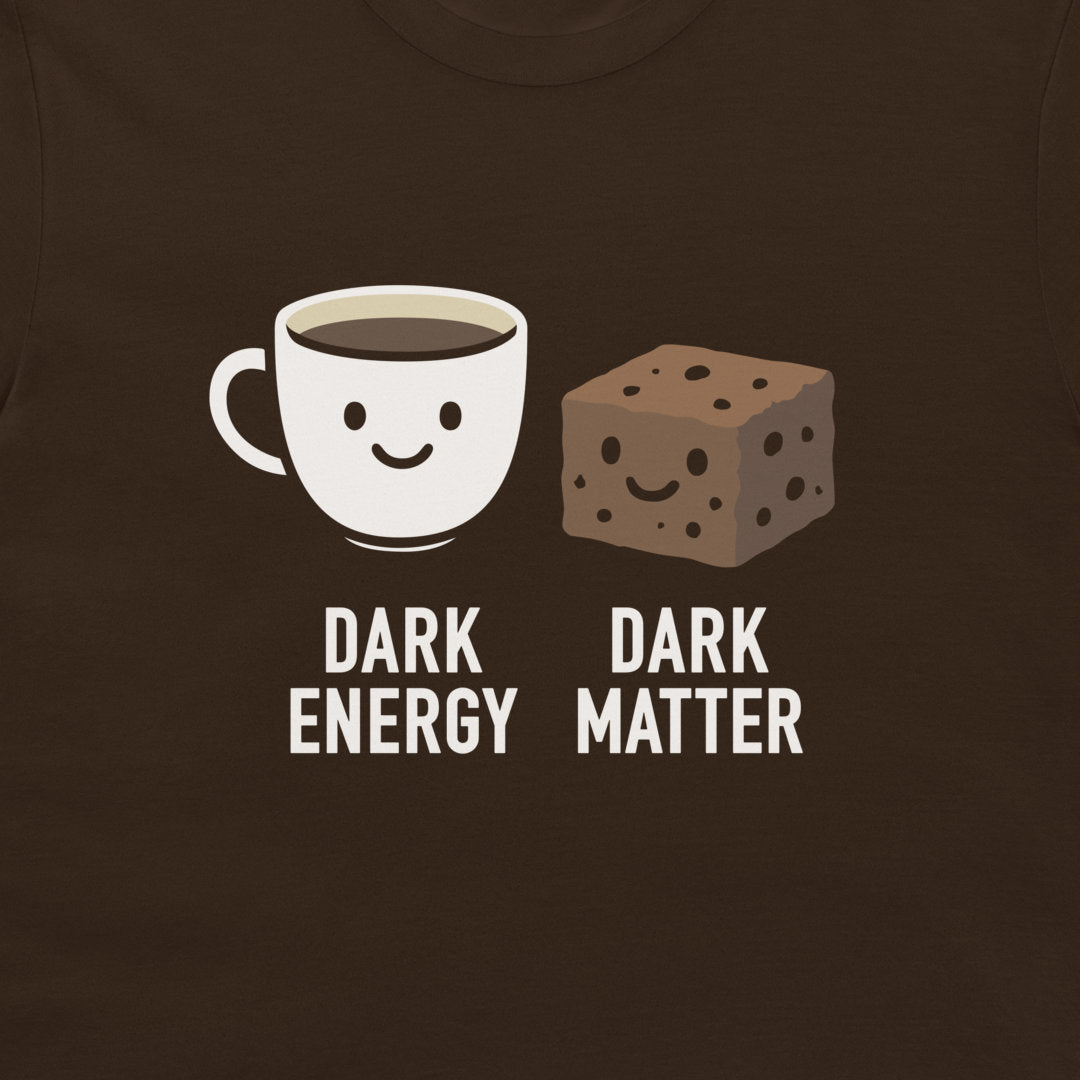 A close-up of a dark brown t-shirt featuring a graphic print of a smiling coffee cup labeled 'DARK ENERGY' next to a smiling chocolate chip cookie labeled 'DARK MATTER'.
